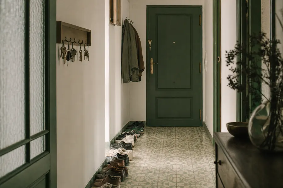 Recibidor de un piso con muchos pares de zapatos alineados junto a la puerta y varios juegos de llaves colgados