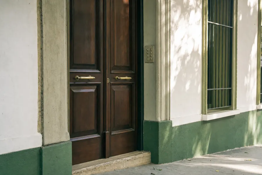 Portal de madera de un edificio de viviendas visto desde la acera, con el portero automático junto a la puerta